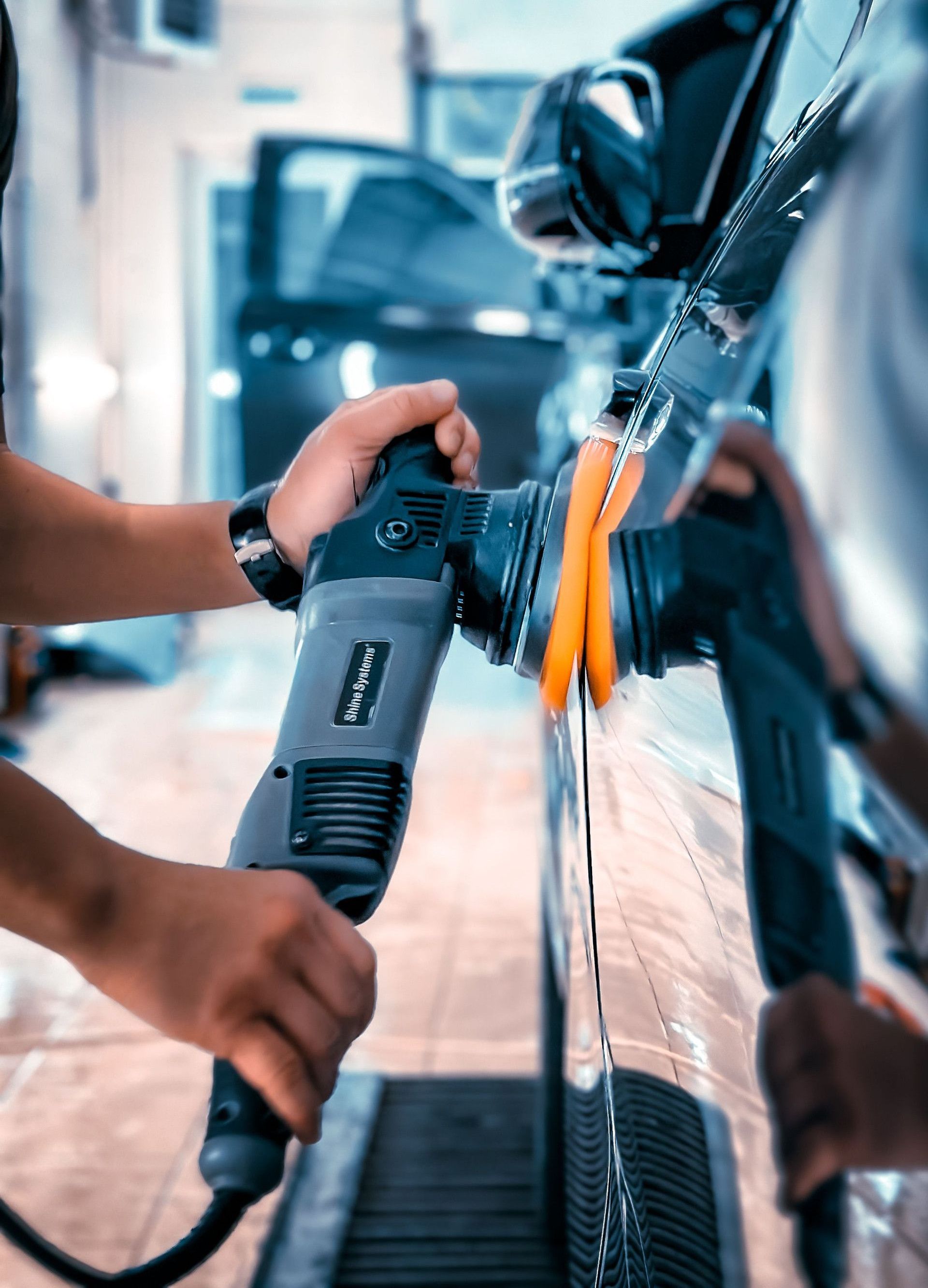 Close-up of a man polishing a car in a garage using an electric buffer tool, showcasing car maintenance.